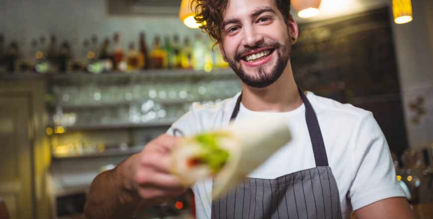 Smiling waiter holding vegetable roll in cafÃ©
